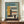 May include: Framed Bauhaus-inspired architectural poster featuring geometric building design in blue, yellow, orange and cream colors with "02" and "Form Follows Function" text, displayed on wooden sideboard next to white ceramic vase and stacked books in neutral-toned room with white walls and crown molding.