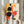 May include: Person holding a framed abstract geometric art print featuring bold circles, rectangles, and lines in black, red, orange, yellow, and blue on cream background. Modern Bauhaus-style composition with overlapping shapes and clean geometric forms. Silver frame, neutral room setting with dried pampas grass and beige curtains visible.
