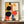 May include: Framed geometric abstract art print in Bauhaus style featuring overlapping black circles, orange and red shapes, blue rectangles, and yellow elements on cream background. Dark wood frame displayed on wooden sideboard with white ceramic vase and stacked books in elegant room with white paneled walls.