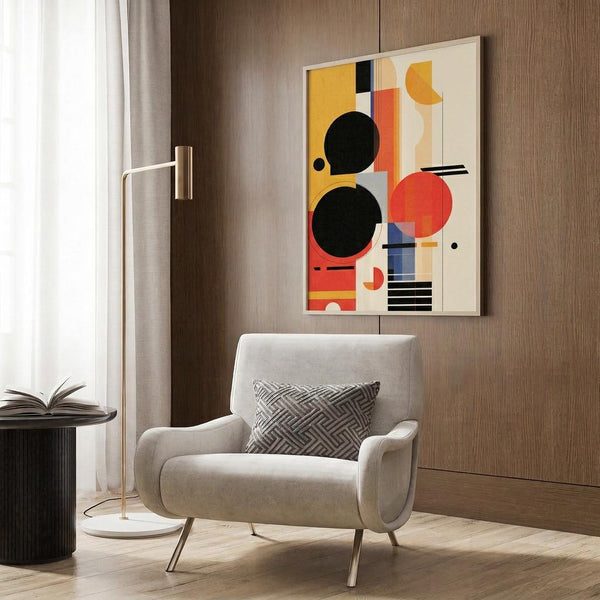 May include: Abstract geometric poster with colorful circles, rectangles and lines in yellow, orange, red, black and blue mounted on wood-paneled wall above beige upholstered armchair with patterned throw pillow. Modern reading nook features brass floor lamp, side table with open book, and white curtains near window.