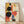 May include: Framed abstract geometric artwork leaning against white wall on light wood floor. Features bold black circles, coral and orange shapes, blue rectangles, and cream background in Bauhaus style. Natural wood frame with warm sunlight casting diagonal shadows across white textured wall.