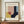 May include: Framed Bauhaus-style geometric art print with abstract shapes in pink, yellow, navy blue, and light blue colors, displayed on wooden sideboard next to white ceramic vase and books in minimalist room setting with white paneled walls