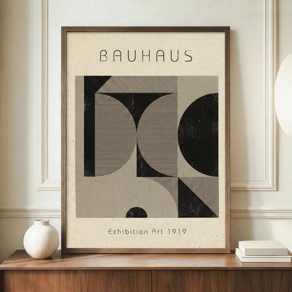 May include: Framed Bauhaus-style art print with geometric black and beige shapes and line patterns, displayed on wooden sideboard next to white ceramic vase and stacked books in neutral-toned room with white paneled walls