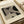 May include: Vintage-style Bauhaus art print displayed on light wooden surface next to white cylindrical object. Print features bold black geometric shapes with diagonal line patterns on cream background, housed in thin brown frame. Text reads "BAUHAUS" at top and "Exhibition Art 1919" at bottom in minimalist sans-serif font.