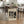 May include: Framed Bauhaus poster with geometric black shapes on cream background, displayed in modern kitchen dining area. Wood table with hairpin legs, wicker and wood chairs, spider plant, wine bottle, and white cup. Light wood floors, white cabinets visible in background.
