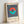 May include: Framed poster with navy blue and white vertical stripes background featuring a split circle design in coral orange and teal green. Text reads "BAUHAUS Exhibition Art 1923" below the geometric design. Light wood frame against white wall with natural lighting casting soft shadows.