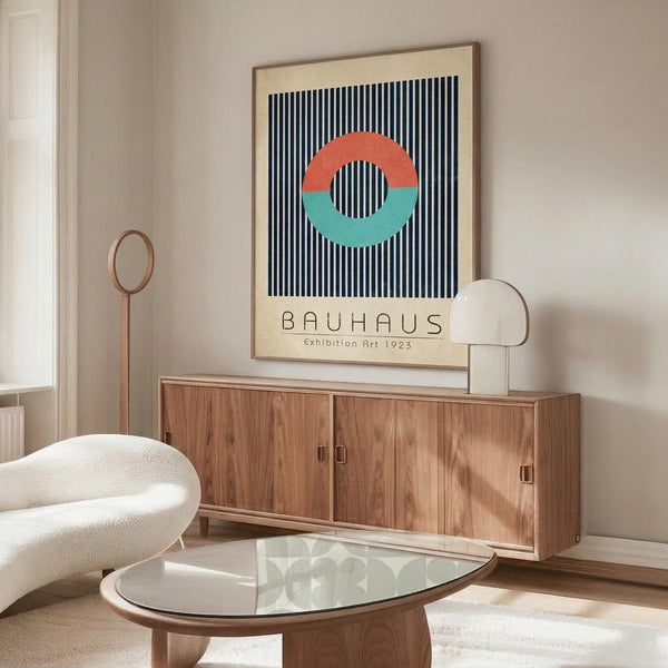 May include: Framed Bauhaus-style poster with coral and teal circle on navy striped background displayed above wooden sideboard in modern living room. White curved chair and glass oval coffee table visible. Poster features clean geometric design with exhibition text below colorful circle motif.