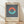 May include: Framed vintage-style poster with geometric design featuring coral and teal semi-circles forming a circle shape over navy blue and white vertical stripes, displayed against white wall on light wood floor with natural lighting casting shadows.