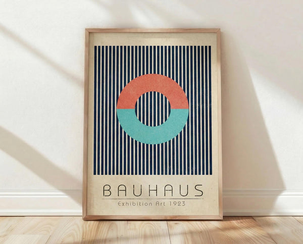 May include: Framed vintage-style poster with geometric design featuring coral and teal semi-circles forming a circle shape over navy blue and white vertical stripes, displayed against white wall on light wood floor with natural lighting casting shadows.