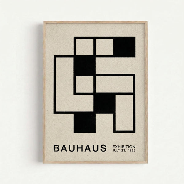 Framed geometric poster with black interlocking rectangular shapes forming an abstract pattern on cream textured background. Features "BAUHAUS" and "EXHIBITION JULY 23, 1923" text at bottom in black sans-serif font. Light wood frame against white wall with subtle shadow.