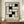 May include: Framed Bauhaus-style poster with black geometric interlocking squares on cream background, displayed on wooden sideboard next to white ceramic vase and stacked books in elegant room with cream walls and white molding.