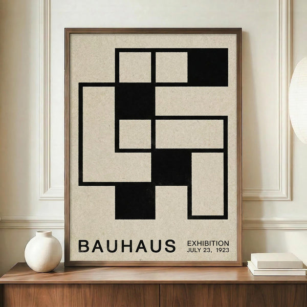 May include: Framed Bauhaus-style poster with black geometric interlocking squares on cream background, displayed on wooden sideboard next to white ceramic vase and stacked books in elegant room with cream walls and white molding.