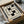 May include: Vintage Bauhaus exhibition poster with geometric black and beige design featuring interlocking rectangular shapes. The minimalist print sits in an open cardboard shipping box surrounded by white tissue paper and wooden dowels, creating an unboxing scene on a neutral surface.