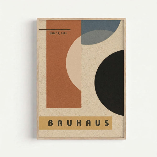 Framed vintage-style poster with geometric abstract design featuring curved and angular shapes in terracotta orange, slate blue, cream, and black on textured beige background. Date "JUNE 17, 1921" appears in upper left, "BAUHAUS" text in yellow banner at bottom. Light wood frame mounted on white wall.