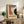 May include: Framed Bauhaus-style poster with abstract geometric shapes in terracotta orange, dusty blue, cream, and dark green, dated June 17, 1921. Displayed on rustic wooden credenza alongside fern plant, ceramic vases, and books in modern living room with neutral walls and leather furniture.