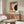 May include: Vintage-style Bauhaus poster with abstract geometric shapes in orange, blue, cream and dark green colors, dated June 17, 1921, displayed above mid-century modern walnut credenza in minimalist living room with white curved chair, glass coffee table, and brass floor lamp