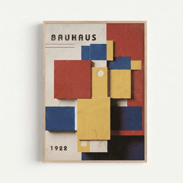 A framed reproduction of a 1922 Bauhaus exhibition poster featuring geometric blocks in primary colors - red, blue, and yellow rectangles arranged in an abstract composition against a cream background. The word "BAUHAUS" appears at the top in bold letters, with "1922" at the bottom. The artwork is displayed in a light wood frame with dimensional paper cutout elements creating shadows and depth. The design exemplifies modernist typography and minimalist color theory.