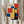 May include: Person holding framed Bauhaus poster with geometric composition of overlapping colored rectangles in red, blue, yellow, and white against cream background. Wood frame, neutral clothing, dried pampas grass visible, soft natural lighting near window with curtains.