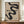 May include: Framed Bauhaus poster with flowing black abstract shapes on beige textured background, displayed on wooden sideboard next to white ceramic vase and stacked books in elegant room with white wainscoting and cream walls. Poster features bold typography reading "BAUHAUS" and "FORM FOLLOWS FUNCTION" with exhibition details for Weimar and Stuttgart locations dated 1919.
