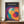 May include: Framed Bauhaus-style poster with overlapping geometric circles in vibrant colors including purple, orange, teal, red, and yellow on dark background, displayed on wooden credenza next to white ceramic vase and stacked books in elegant room with white wainscoting.