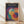 May include: Framed Bauhaus-style poster with overlapping translucent circles in vibrant colors including blue, purple, red, orange, yellow, and teal on dark background. Light wood frame leaning against white wall on light wooden floor with natural window shadows.