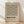 May include: Framed geometric poster with black linear zigzag pattern on cream background, displaying "BAUHAUS" text and German description below. Light wood frame leaning against white wall corner on natural wood flooring with soft natural lighting and shadows.