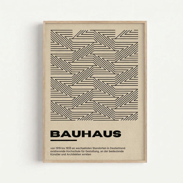 Framed geometric art print featuring black linear zigzag and chevron patterns on cream paper, displayed against a white wall. The design shows interlocking angular shapes created with thin parallel lines forming a repeating tessellation. Below the pattern is bold "BAUHAUS" text with German descriptive text underneath. The piece is housed in a natural wood frame with visible grain.