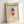 May include: Framed Bauhaus poster with geometric diamond shapes in blue and red overlapping with black outlines on cream background. Light wood frame leaning against white wall in bright natural lighting. Vintage-style art print featuring "Geometry and Simplicity" subtitle and German exhibition text at bottom.