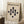 May include: Framed Bauhaus poster with cream textured background and black geometric shapes arranged vertically - circles and elongated teardrop forms. Black text reads "BAUHAUS" and "GEOMETRY AND SIMPLICITY" at top, with German text at bottom referencing Weimar and Stuttgart locations. Light wood frame, displayed leaning against white wall corner on textured rug, with coffee cup on wooden block nearby.