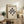 May include: Framed Bauhaus poster with geometric black shapes on cream background, displayed on rustic wooden sideboard alongside fern plant, ceramic vase, and books in neutral-toned living room setting with beige chair and soft lighting