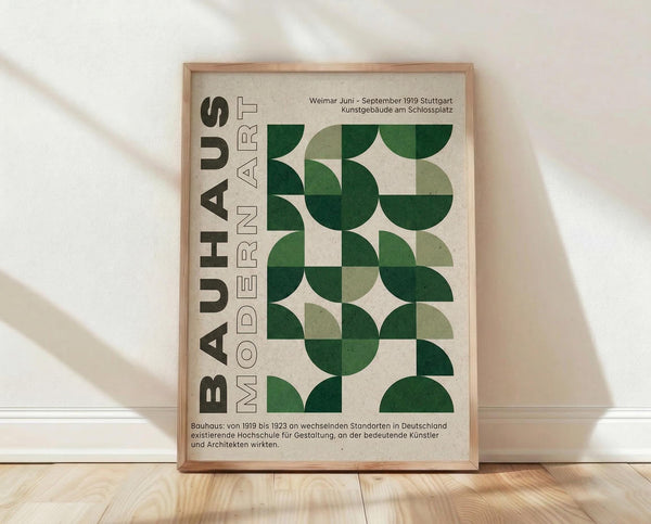 May include: Framed Bauhaus poster with green geometric semicircle pattern and German text, displayed on light wooden floor against white wall with natural shadows. The design features various shades of green circles and half-circles arranged in a grid pattern on cream background, housed in natural wood frame.