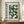 May include: Framed Bauhaus-style poster with green geometric semicircles arranged in a grid pattern on cream background, displayed on wooden sideboard next to white ceramic vase and stacked books in room with white paneled walls and warm lighting.