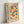 May include: A framed poster with geometric design featuring colorful semicircles and quarter circles in red, orange, blue and yellow arranged in a grid pattern. Text reads "BAUHAUS MODERN ART" vertically on left side, with German text about Weimar 1919 Stuttgart exhibition. Light wood frame leaning against white wall on white surface.