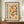 May include: Framed Bauhaus-style poster with geometric circles and semicircles in orange, red, blue, and yellow arranged in a grid pattern. German text reads "BAUHAUS MODERN ART" vertically on left side. Cream-colored background with vintage texture. Dark wood frame displayed on wooden sideboard next to white ceramic vase and stacked books in bright room with white walls and molding.