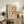 May include: Framed Bauhaus-inspired poster with geometric circles and semicircles in orange, blue, red, and yellow tones, displayed on rustic wooden sideboard alongside fern plant, pottery vase, stacked books, and leather armchair in neutral-toned living room setting