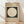 May include: Framed Bauhaus poster with beige background and dark green square containing large cream circle, displayed on light wood floor against white wall with natural lighting creating soft shadows across the scene