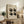 May include: Framed Bauhaus poster with beige background and geometric black and gray shapes arranged in a grid pattern, dated 1919 with German text below. Displayed on rustic wooden sideboard alongside fern plant, books, ceramic vase, and leather chair in neutral-toned living room setting.