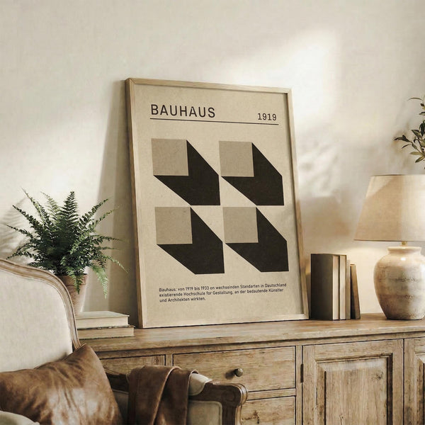 May include: Framed Bauhaus poster with beige background and geometric black and gray shapes arranged in a grid pattern, dated 1919 with German text below. Displayed on rustic wooden sideboard alongside fern plant, books, ceramic vase, and leather chair in neutral-toned living room setting.