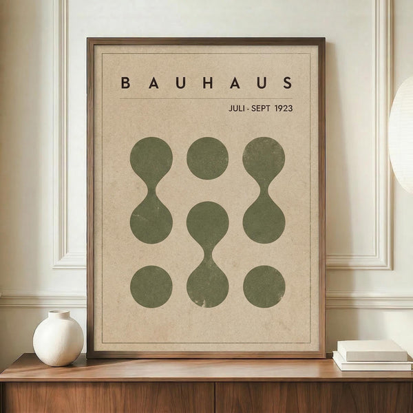 May include: Framed vintage-style Bauhaus poster with beige background and green geometric circles arranged in a 3x3 grid pattern, displayed on wooden credenza alongside white ceramic vase and stack of books in neutral-toned room with white wainscoting