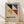 May include: Framed geometric poster with colorful triangular shapes in black, blue, yellow and red on cream background, displayed against white wall on wooden floor with natural lighting and shadow patterns