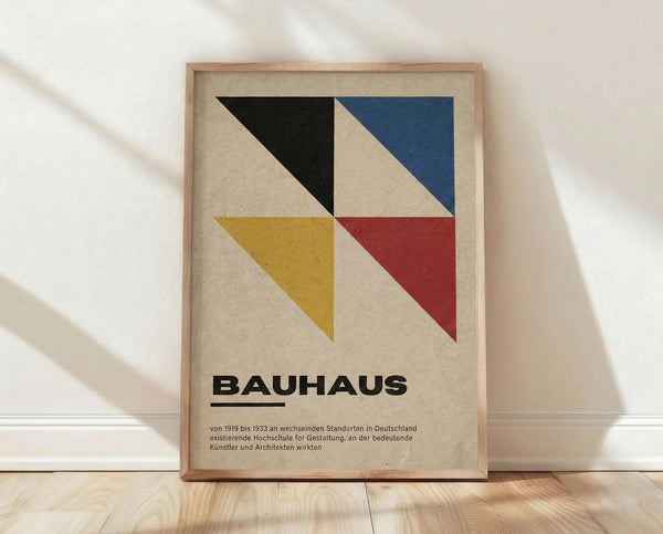 May include: Framed geometric poster with colorful triangular shapes in black, blue, yellow and red on cream background, displayed against white wall on wooden floor with natural lighting and shadow patterns
