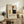 May include: Framed Bauhaus poster with geometric abstract design featuring colored rectangles in red, blue, yellow, and black on cream background, displayed on rustic wooden sideboard alongside fern plant, ceramic vase, and books in cozy living room setting with beige armchair and neutral wall