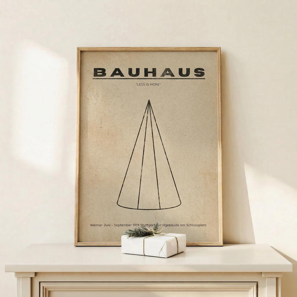 May include: Framed Bauhaus poster with beige background featuring black geometric cone design and "LESS IS MORE" text, displayed on light wood console table beside white wrapped gift with natural twig decoration against cream wall
