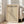 May include: Minimalist Bauhaus poster in beige wooden frame leaning against white wall next to cream sofa. Features geometric cone design with "LESS IS MORE" motto on vintage beige background. German text references Weimar and Stuttgart 1919. Natural lighting from windows creates soft shadows on light wooden floor.