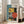 May include: Large framed poster with geometric Bauhaus-style design featuring teal, yellow, coral, and black shapes including circles, rectangles, and linear elements. Number "01" appears in corner with "BAUHAUS" text vertically along left side. Light wood frame leans against white wall next to beige sofa in bright, minimalist living room with windows.
