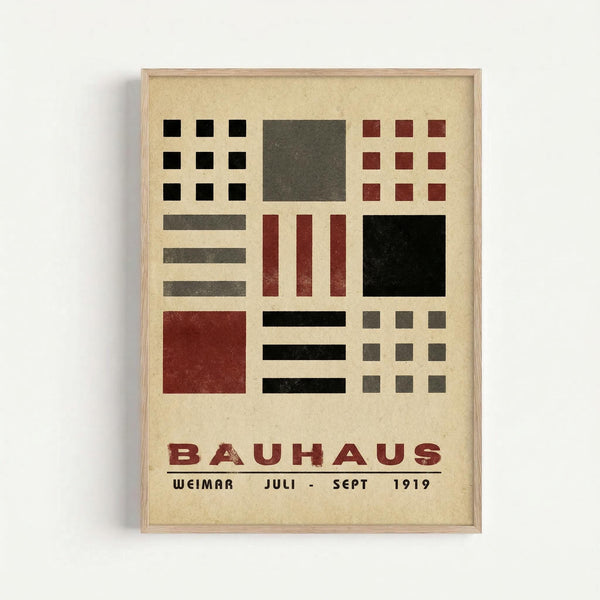 A framed vintage Bauhaus poster featuring geometric shapes in black, red, and gray arranged in a grid pattern on cream paper. The minimalist design includes squares, rectangles, and horizontal bars in the characteristic Bauhaus style. Text at bottom reads "BAUHAUS WEIMAR JULI - SEPT 1919" in red lettering. The poster is displayed in a simple light wood frame against a white wall background.