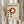 May include: Person holding framed Bauhaus poster with geometric design featuring rust red circle and black dots on cream background, displayed next to dried pampas grass against neutral curtained window setting
