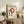 May include: Framed Bauhaus poster with cream background featuring black text, red circular design, and black dots arranged in geometric pattern. Displayed on rustic wooden sideboard with books, ceramic vase, and fern plant. Neutral living room setting with beige chair and brown throw pillows visible.
