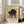 May include: Framed art print leaning against beige chair in bright living room with white walls and windows. Print shows black cat in arched, hissing pose on tan background with Japanese characters and museum text. Light wood frame, approximately 2-3 feet tall, casting soft shadow on hardwood floor.