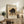 May include: Framed vintage-style poster featuring a black cat with arched back in defensive pose on beige background, displayed on rustic wooden sideboard alongside fern plant, books, and ceramic vase in neutral-toned living room setting with cream upholstered chair visible.